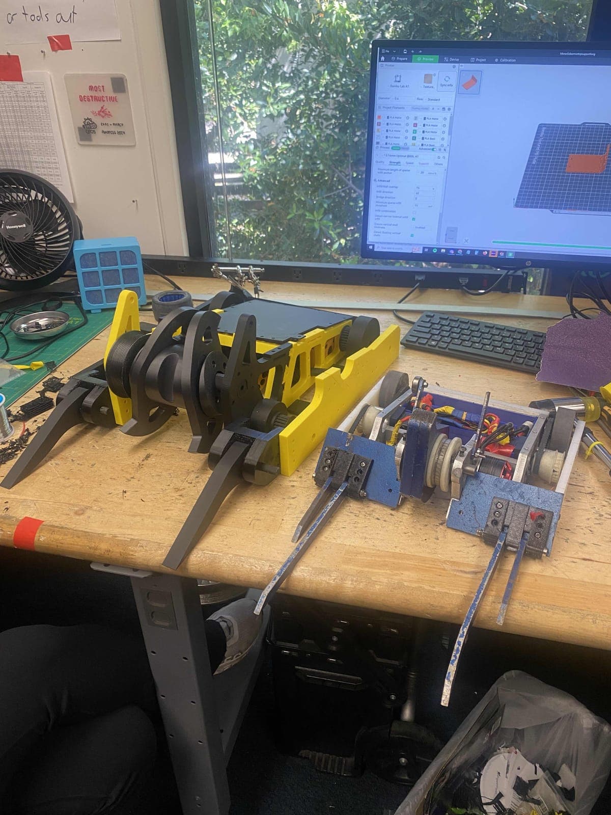 The 3D-printed Shear Force prototype in yellow and black on a workbench, next to a smaller 12 lb robot