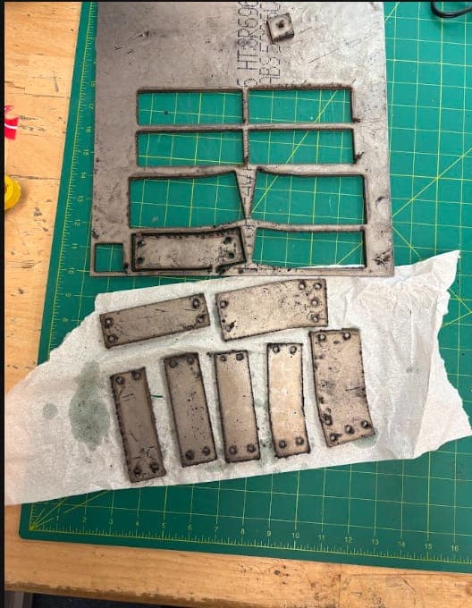 Plasma-cut titanium side armor supports on a cutting mat